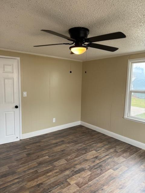 spare room with ornamental molding, a textured ceiling, dark wood-style floors, baseboards, and ceiling fan