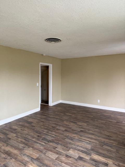 spare room with visible vents, baseboards, a textured ceiling, and dark wood finished floors