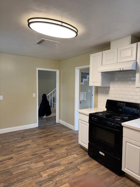 kitchen featuring visible vents, dark wood-style floors, white cabinetry, black gas range oven, and light countertops