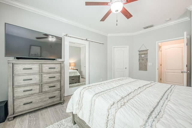 bedroom with a ceiling fan, wood finished floors, visible vents, ornamental molding, and a barn door