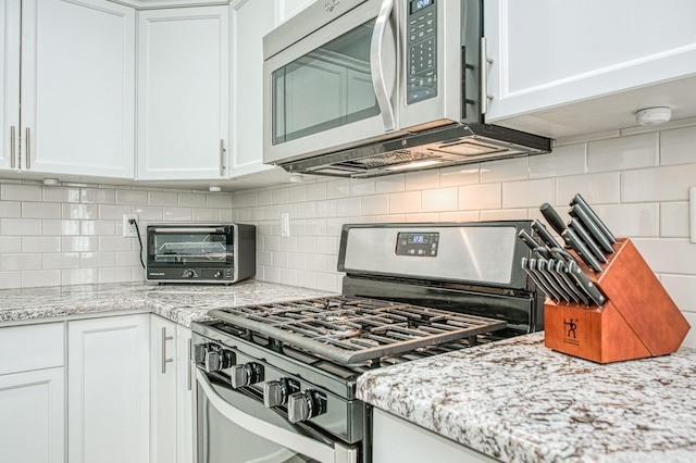 kitchen featuring decorative backsplash, white cabinetry, stainless steel appliances, and light stone countertops