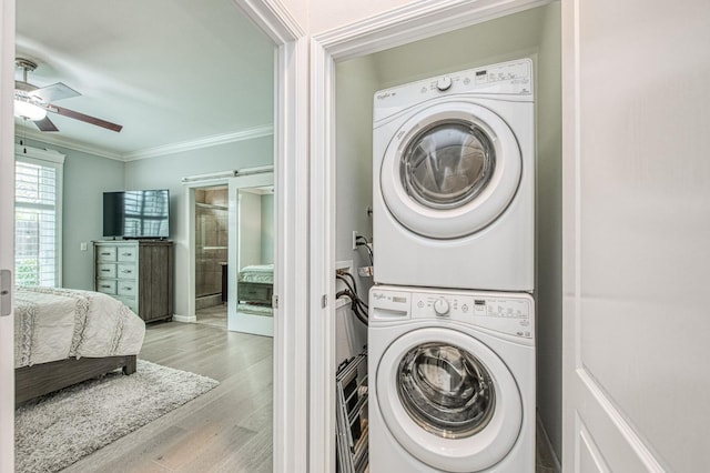 laundry room featuring wood finished floors, stacked washing maching and dryer, laundry area, ceiling fan, and crown molding