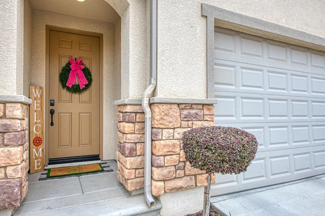 entrance to property with a garage, stone siding, and stucco siding