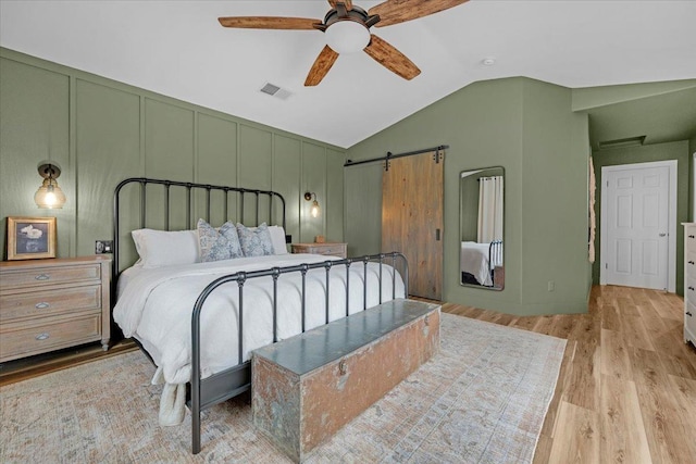 bedroom featuring visible vents, a barn door, lofted ceiling, wood finished floors, and a decorative wall