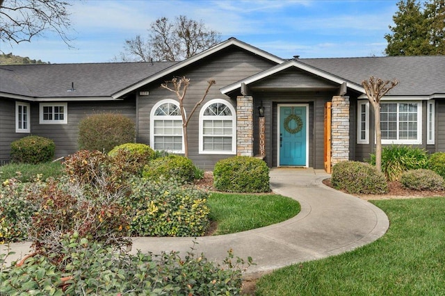 ranch-style home featuring stone siding, a front yard, and roof with shingles