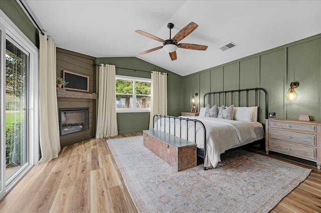 bedroom featuring visible vents, vaulted ceiling, a fireplace, wood finished floors, and a decorative wall