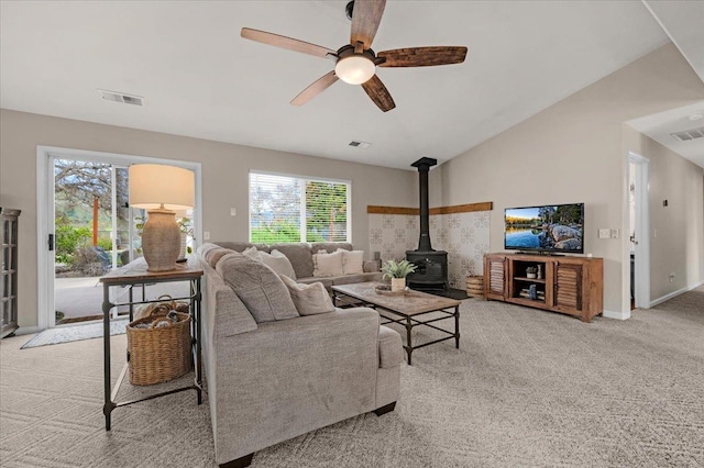 living room with a ceiling fan, a wood stove, plenty of natural light, vaulted ceiling, and light carpet