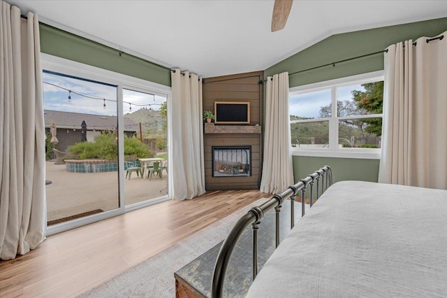 bedroom featuring a ceiling fan, access to outside, wood finished floors, a fireplace, and lofted ceiling