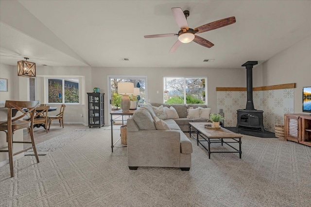 living area with light carpet, visible vents, a wood stove, and ceiling fan