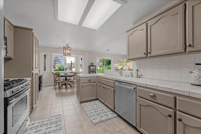 kitchen with a wealth of natural light, appliances with stainless steel finishes, a peninsula, and light tile patterned flooring