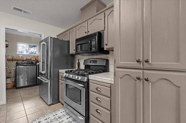 kitchen with visible vents, tile countertops, appliances with stainless steel finishes, light tile patterned flooring, and washer / dryer