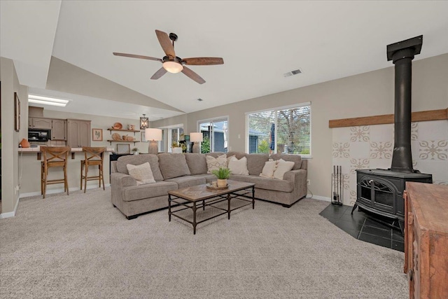 living area with visible vents, ceiling fan, lofted ceiling, light carpet, and a wood stove