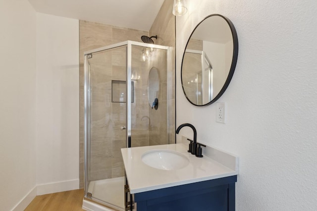 bathroom with a shower stall, vanity, baseboards, and wood finished floors