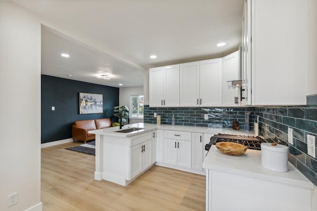 kitchen featuring decorative backsplash, light wood-style flooring, a peninsula, and a sink