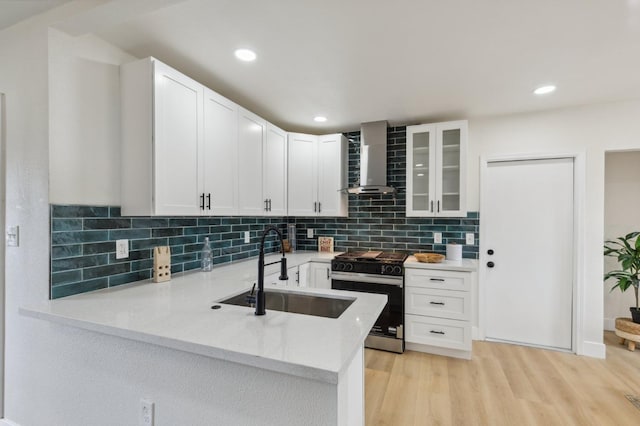 kitchen featuring stainless steel gas range oven, light wood-style flooring, a sink, a peninsula, and wall chimney range hood