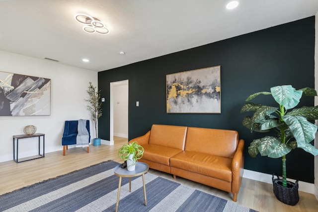 living room with visible vents, wood finished floors, recessed lighting, baseboards, and an accent wall