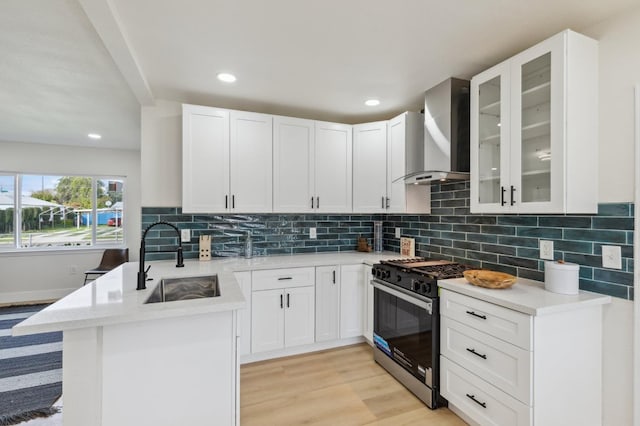 kitchen with light countertops, gas range oven, a peninsula, wall chimney exhaust hood, and a sink