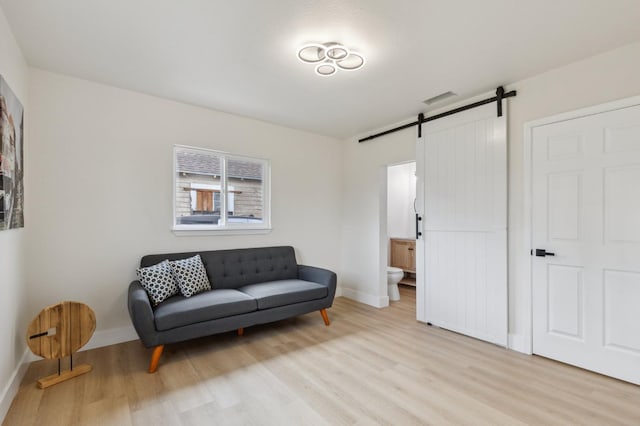 sitting room with visible vents, light wood-style flooring, baseboards, and a barn door