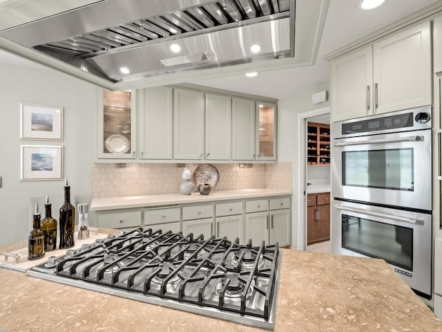 kitchen with cooktop, double oven, wall chimney exhaust hood, and decorative backsplash