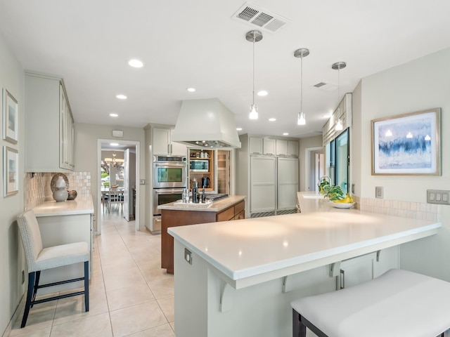 kitchen with visible vents, a kitchen bar, double oven, a peninsula, and decorative backsplash