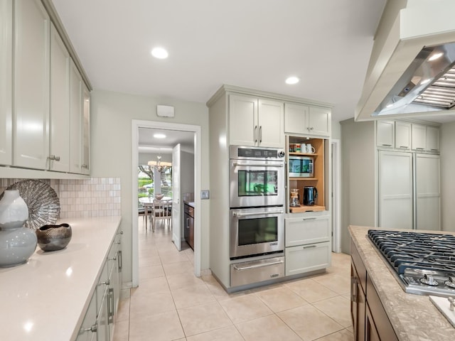 kitchen featuring decorative backsplash, light countertops, appliances with stainless steel finishes, a warming drawer, and wall chimney exhaust hood