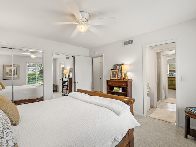 bedroom featuring visible vents, light carpet, two closets, a ceiling fan, and baseboards