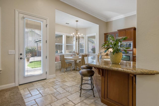 kitchen featuring stone tile floors, light stone counters, stainless steel appliances, crown molding, and decorative light fixtures