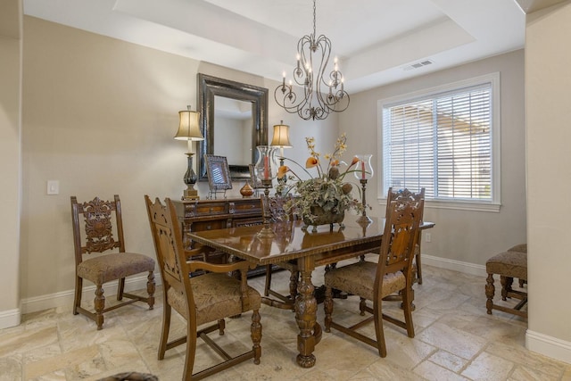 dining room featuring visible vents, baseboards, a tray ceiling, stone tile flooring, and a notable chandelier