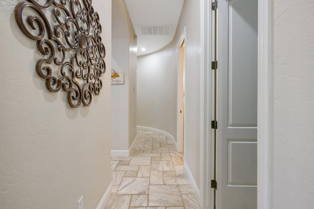 corridor featuring stone tile floors, baseboards, and visible vents