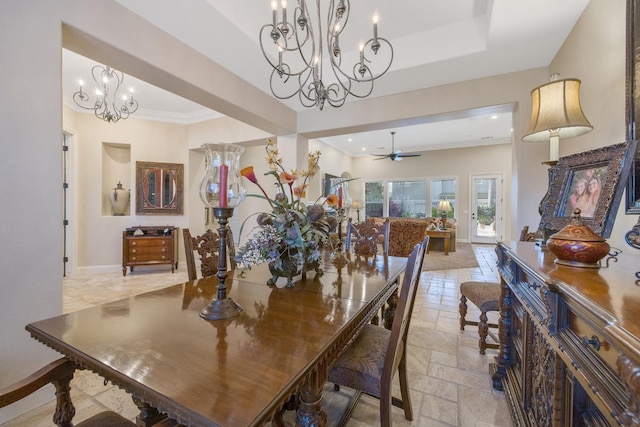 dining space with stone tile floors, baseboards, a tray ceiling, crown molding, and ceiling fan with notable chandelier