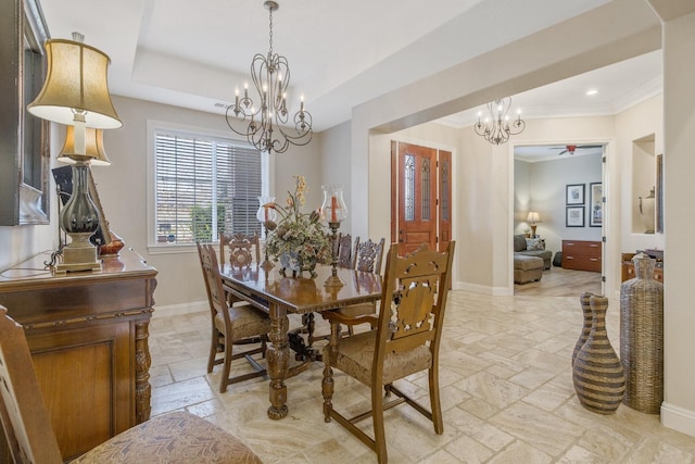 dining room featuring baseboards, a tray ceiling, stone tile flooring, crown molding, and a notable chandelier