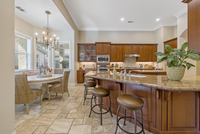 kitchen with visible vents, under cabinet range hood, a breakfast bar area, appliances with stainless steel finishes, and stone tile flooring