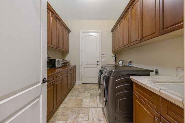 laundry room with baseboards, washing machine and clothes dryer, a toaster, cabinet space, and stone tile flooring