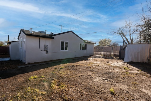 back of property featuring an outdoor structure, fence, a shed, and stucco siding