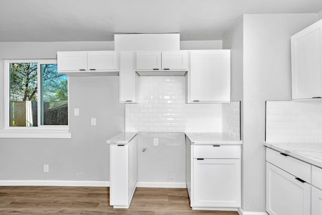 kitchen with light stone counters, decorative backsplash, light wood finished floors, and white cabinetry