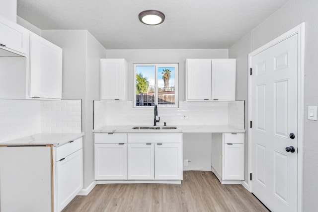 kitchen with white cabinetry, decorative backsplash, light wood-style flooring, and a sink