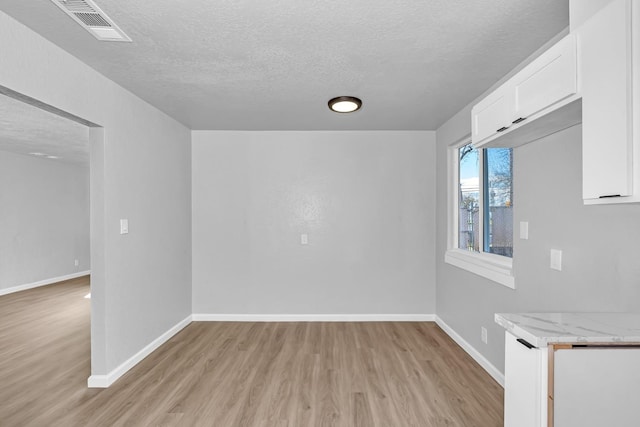 empty room featuring visible vents, baseboards, light wood-style floors, and a textured ceiling