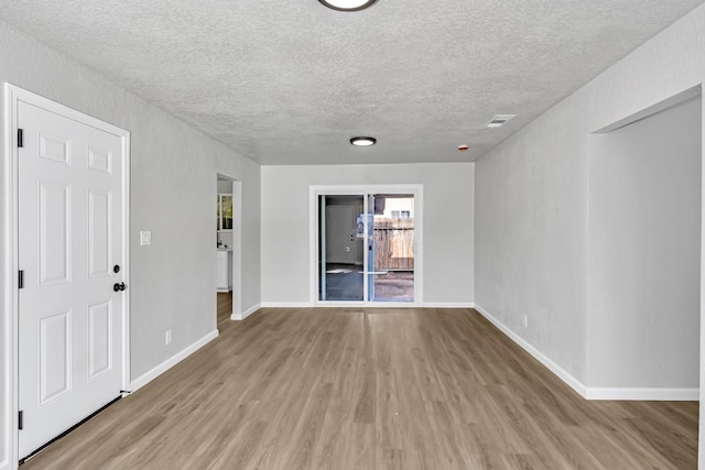 spare room with visible vents, light wood-style flooring, a textured ceiling, and baseboards