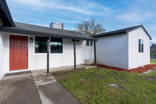 doorway to property with a shingled roof, a yard, and stucco siding