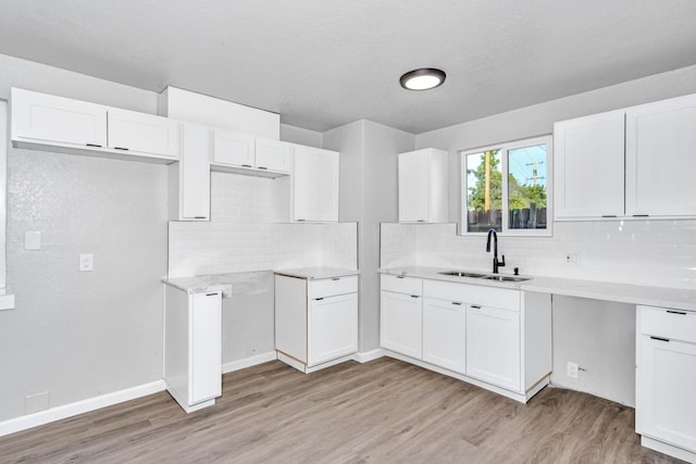 kitchen with light wood-type flooring, a sink, backsplash, white cabinetry, and light countertops