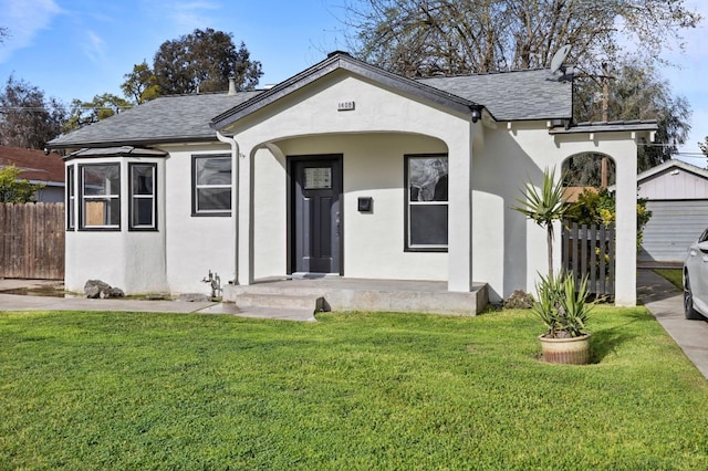 view of front of property featuring a front lawn, fence, roof with shingles, and stucco siding