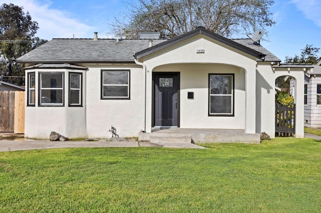 view of front facade featuring a shingled roof, a front lawn, fence, and stucco siding