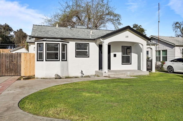 view of front of house with a front lawn, fence, a porch, roof with shingles, and stucco siding