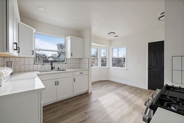 kitchen with gas stove, light wood finished floors, a sink, decorative backsplash, and a wealth of natural light