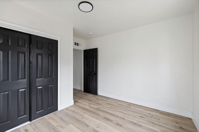 unfurnished bedroom featuring visible vents, baseboards, a closet, and wood finished floors