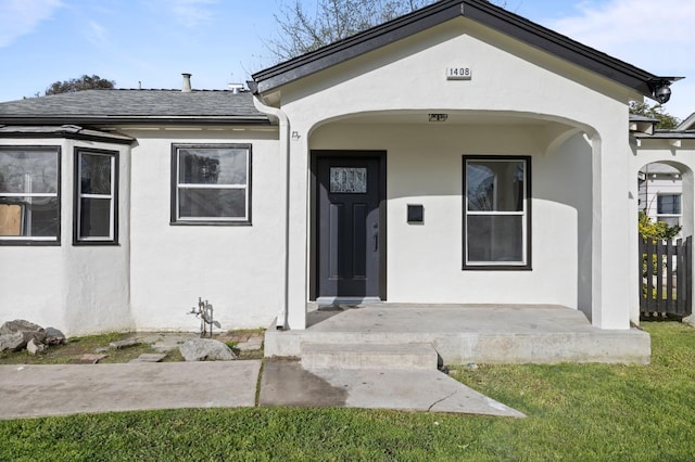 view of exterior entry with roof with shingles and stucco siding