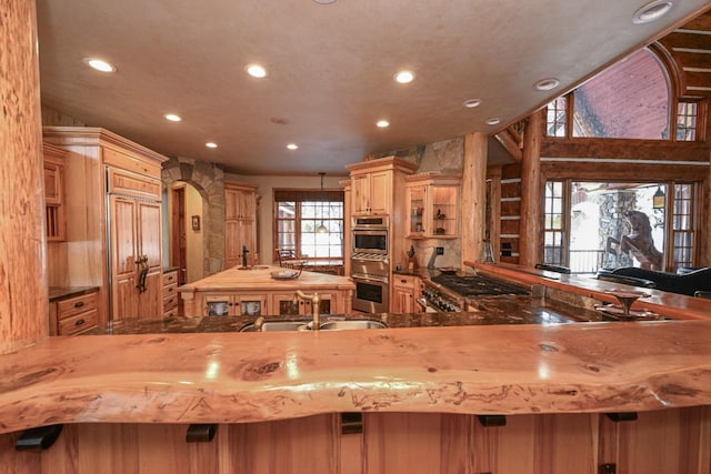 kitchen featuring recessed lighting, appliances with stainless steel finishes, a peninsula, arched walkways, and a sink