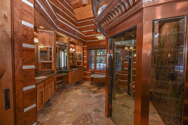 full bath featuring a tub to relax in, two vanities, a stall shower, stone finish floor, and a sink