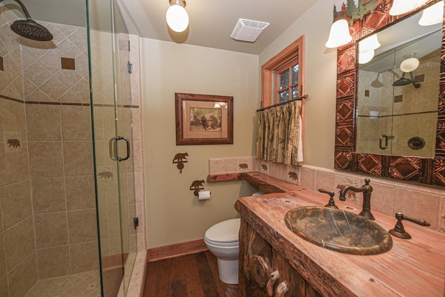 bathroom with visible vents, toilet, wood finished floors, a shower stall, and vanity