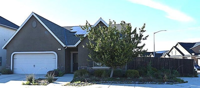 view of front of home with fence, solar panels, an attached garage, concrete driveway, and stone siding